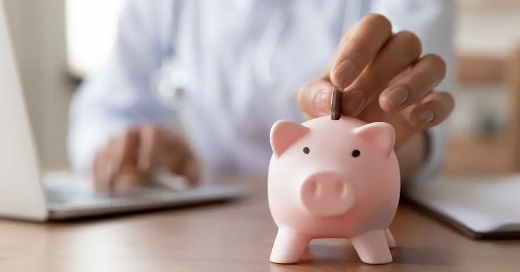 close-up-of-female-doctor-hand-put-money-in-piggybank