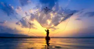 asian-fisherman-on-wooden-boat-casting-a-net-for-catching-freshwater-fish